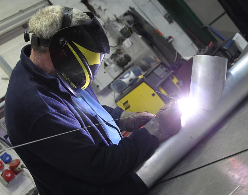 A man welding a piece of metal in a factory while filling out an order form.