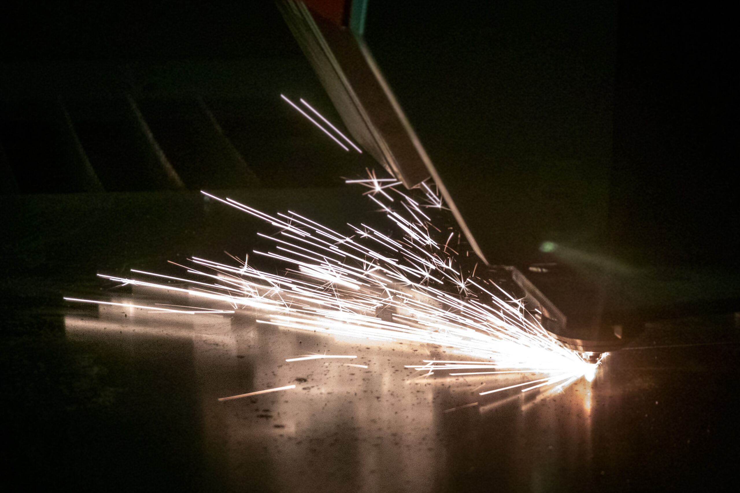 A man is laser cutting metal sheets with sparks in the dark.