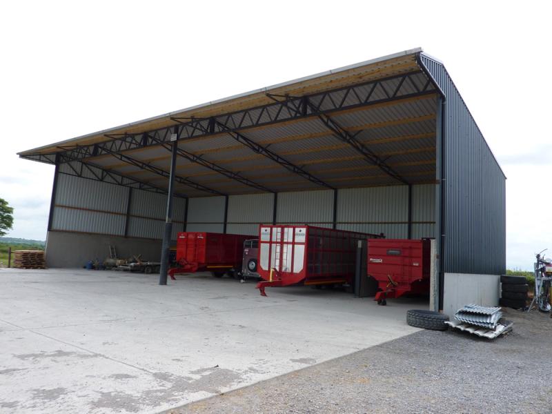 A large barn with two red trailers parked in it, belonging to steel manufacturers.