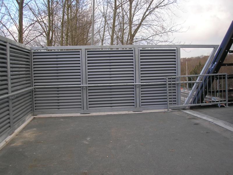 A steel fence with shutters in the middle of a parking lot.