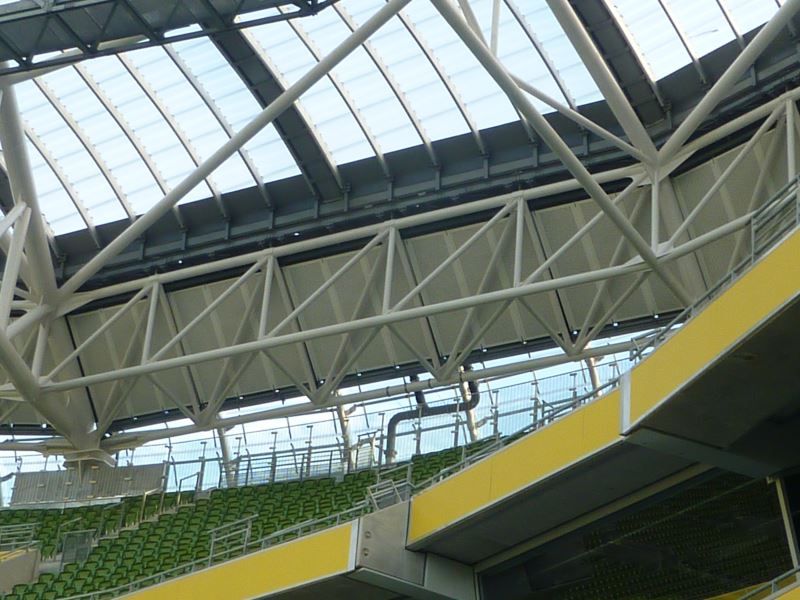 A stadium with green seats and a metal roof.