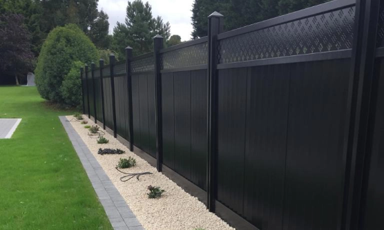 A black, privacy fence lining a landscaped area with small shrubs and white pebbles.